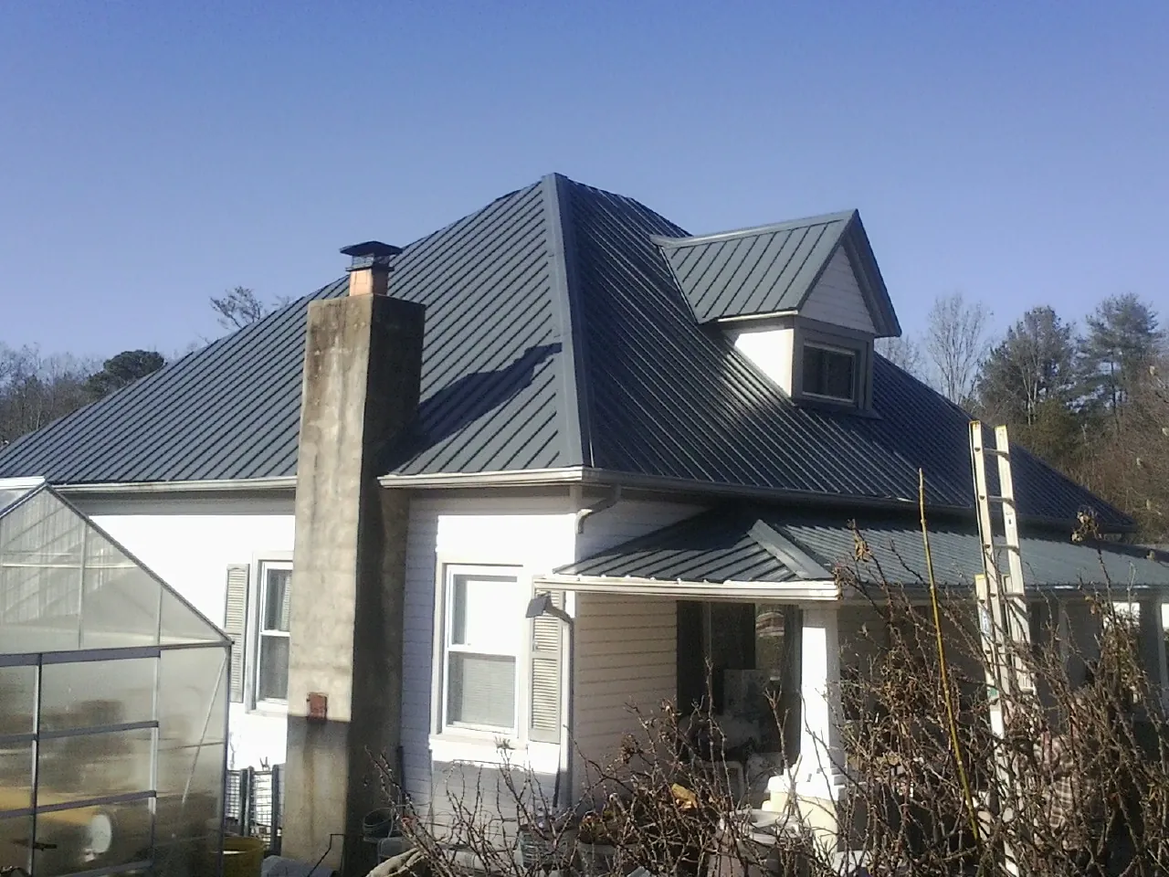 Dark blue standing seam metal roof on a white farmhouse with dormer — Slate & Tile Roof Repair by Roofing Brothers in Madrid