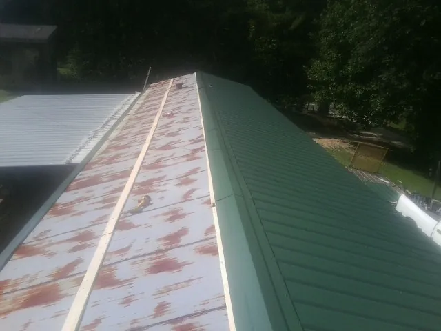 Old rusted panels beside newly installed green metal roofing — Wind Damage Roof Repair by Roofing Brothers in Madrid