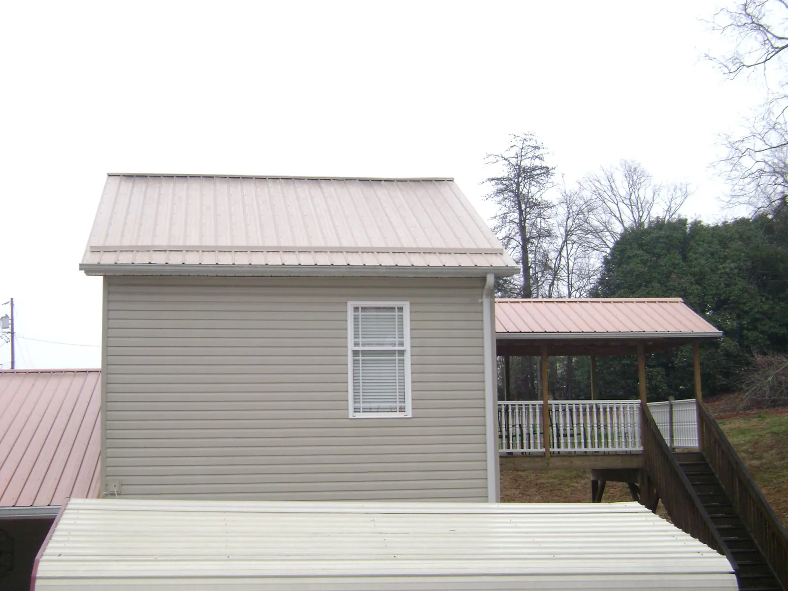 Tan metal roofs on a two story addition and attached porch, from a Roof Replacement job in Madrid